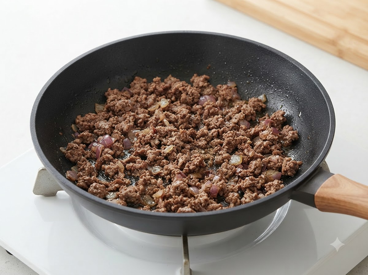 Gegartes Hackfleisch und Zwiebeln, die in einer Bratpfanne miteinander vermischt sind.