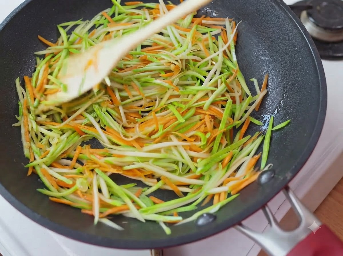Geraspelte Zucchini und Karotten sind gleichmäßig in einer kreisförmigen Schicht in der Pfanne verteilt.