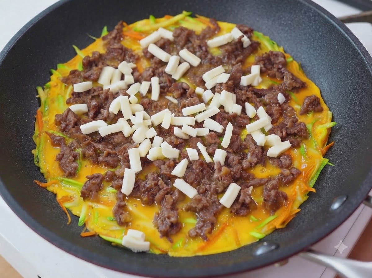 Geriebener Mozzarella-Käse wird über die Rindfleisch- und Eierschicht in der Pfanne gestreut.