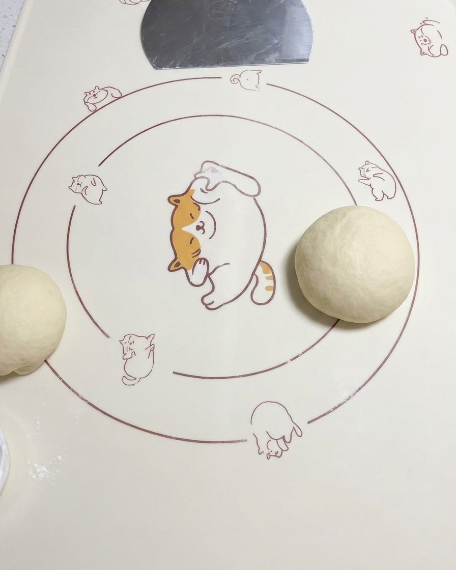 Eine runde Teigkugel liegt auf einer Silikonmatte neben einem weiteren ausgerollten Teigstück.