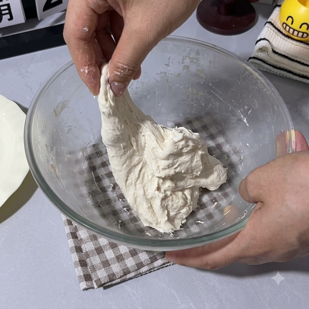 Eine Hand zieht und faltet den klebrigen Teig in der Glasschüssel nach oben.