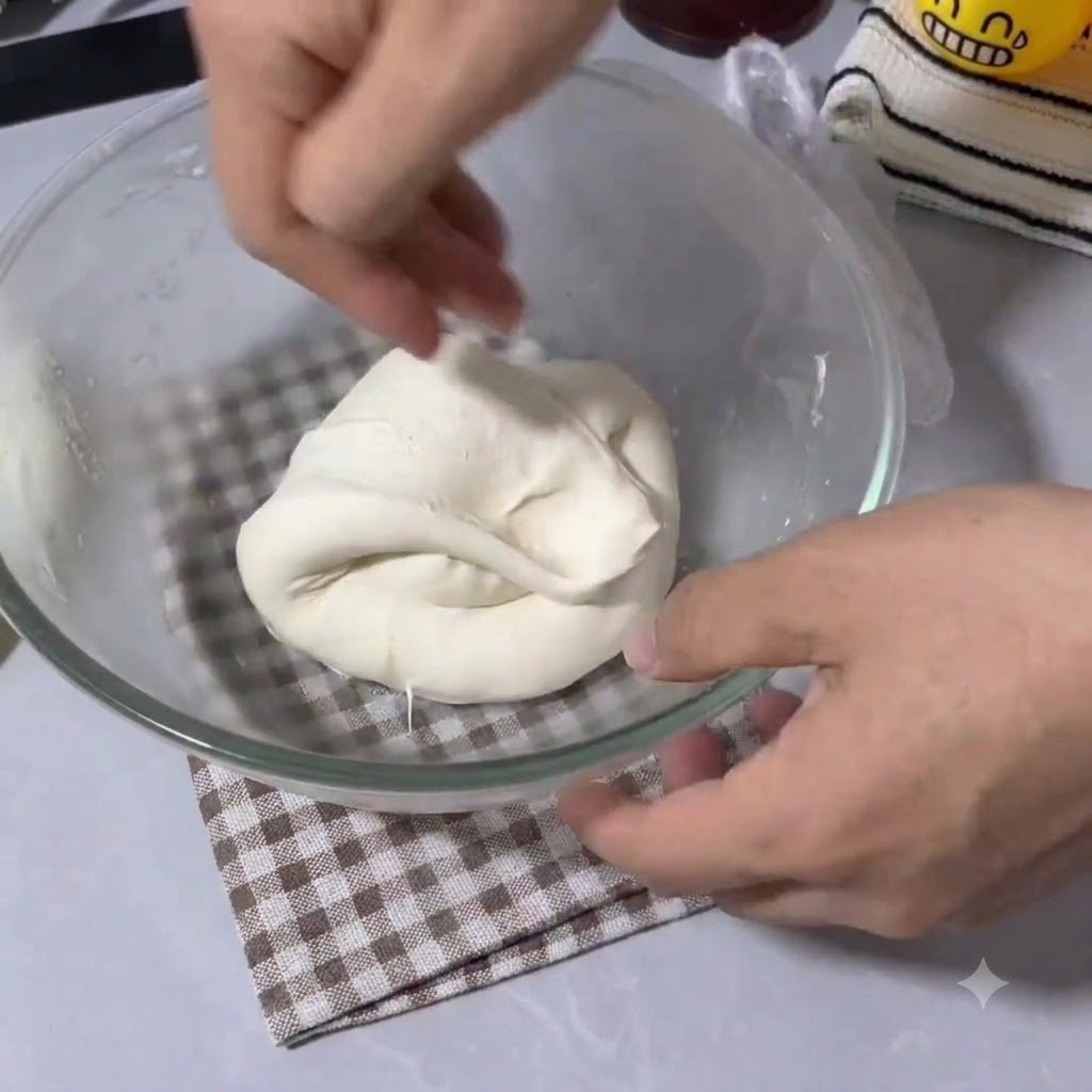 Hände falten und dehnen elastischen Pizzateig in einer klaren Glasschüssel.
