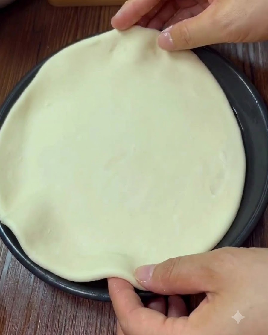 Hände formen und kneifen den Rand eines runden Pizzateigs in einer Backform.