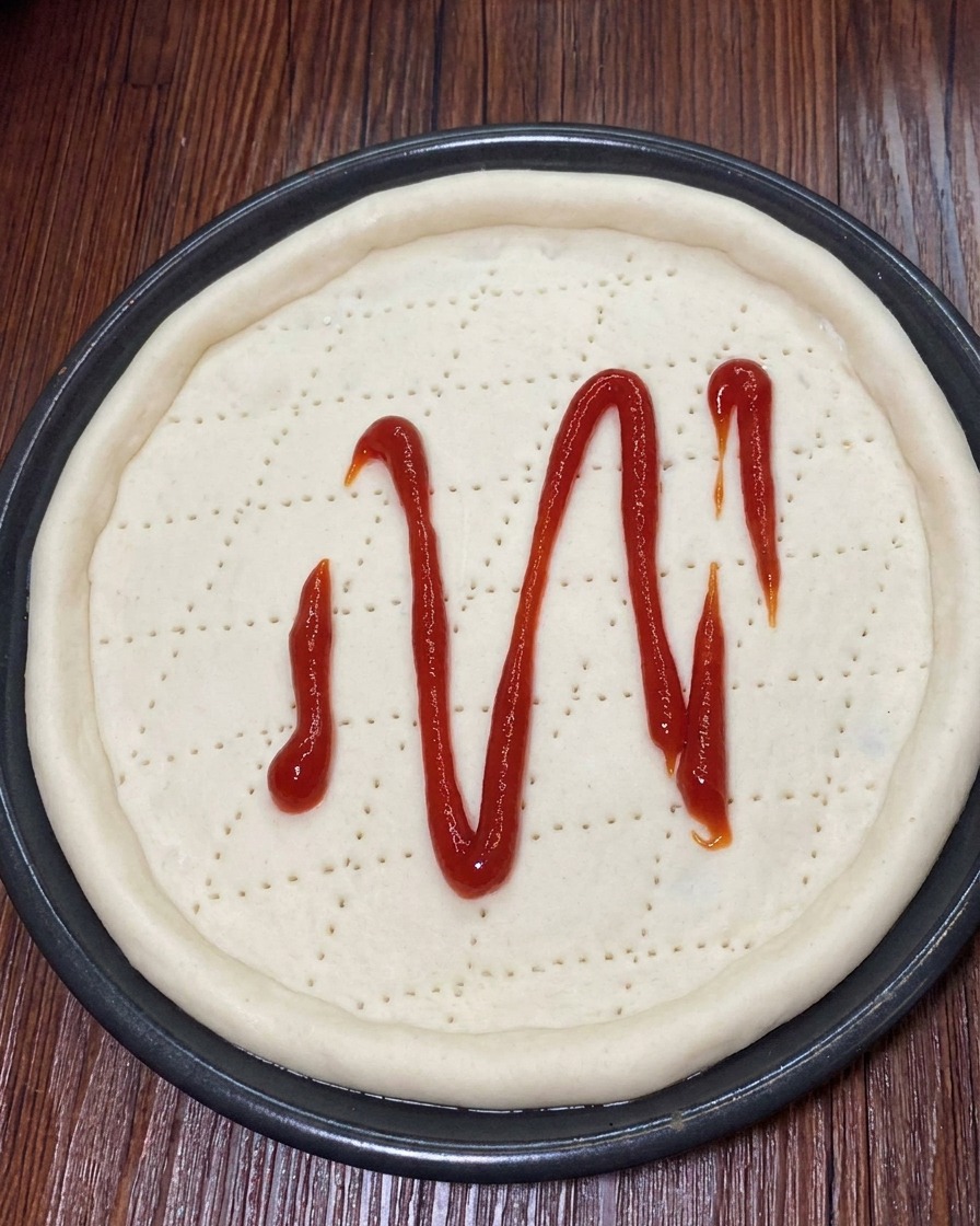 Geriebener Mozzarella wird gleichmäßig über die Tomatensoße auf dem Pizzateig gestreut.
