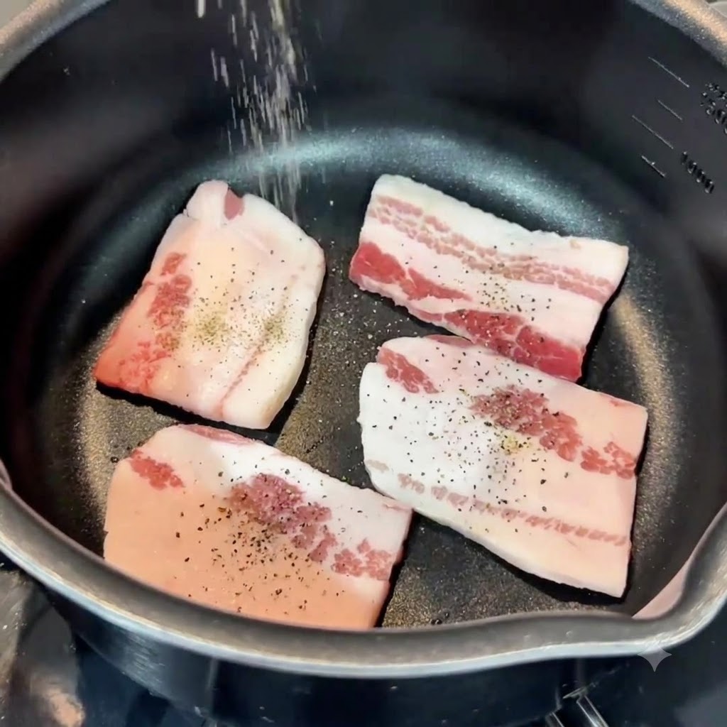 Salz und Pfeffer werden von oben auf Schweinebauchscheiben in einer Panne gestreut.