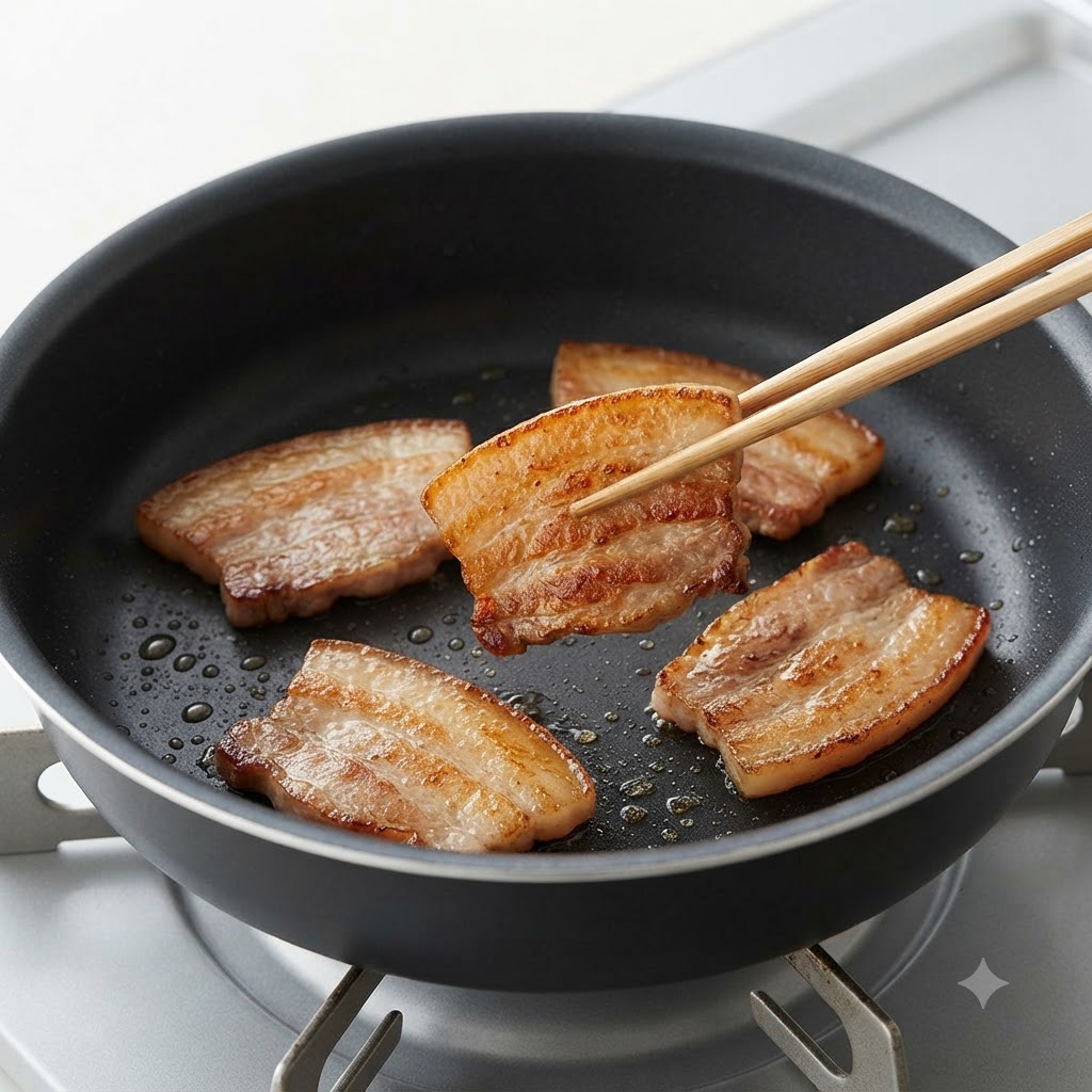 Ein paar Essstäbchen wenden eine gebräunte und angebratene Scheibe Schweinebauch in einer Pfanne.