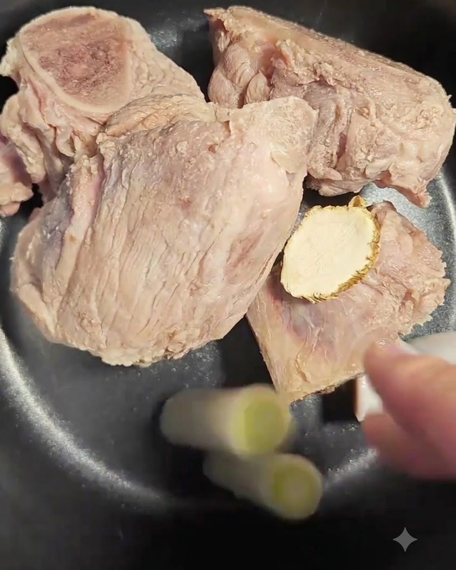 Zwei Stücke Lauchzwiebelweiß werden in den Topf mit Knochen und Angelikawurzel gegeben.