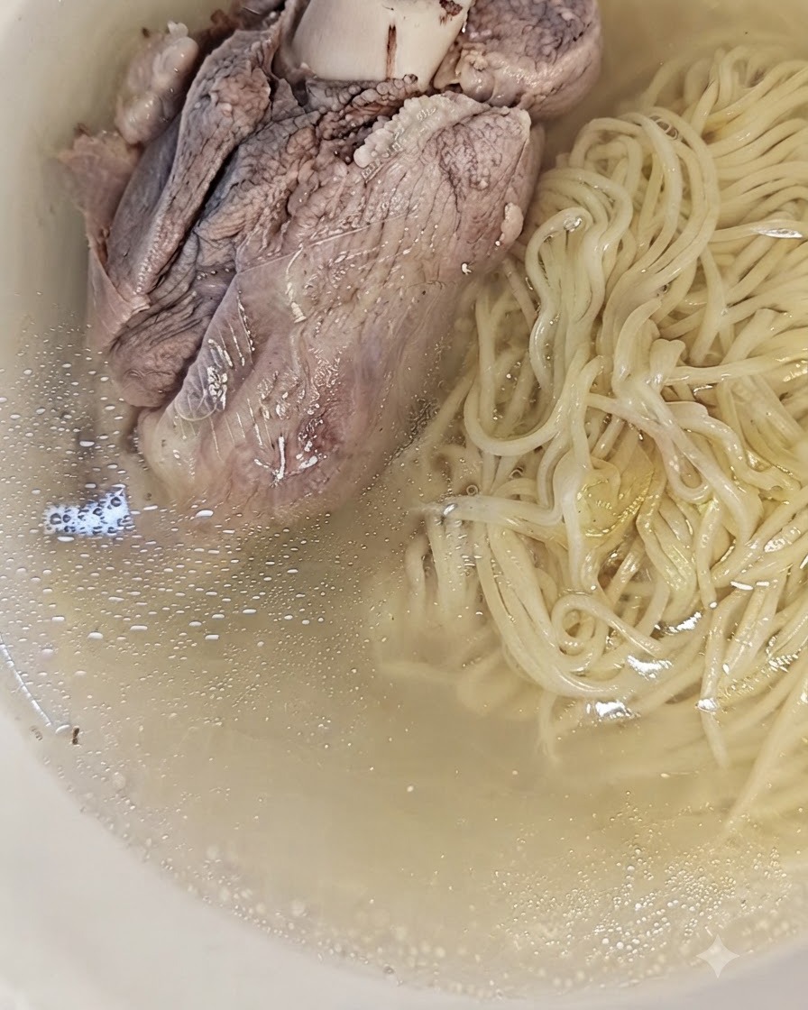 Ein großer gekochter Schweineknochen auf den Nudeln und der Brühe in einer Schüssel, servierfertig.