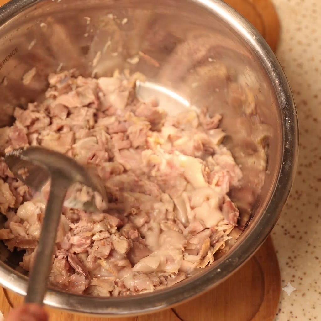 Gekochtes Schweinefleisch wird in einer großen Rührschüssel gründlich zerstampft.