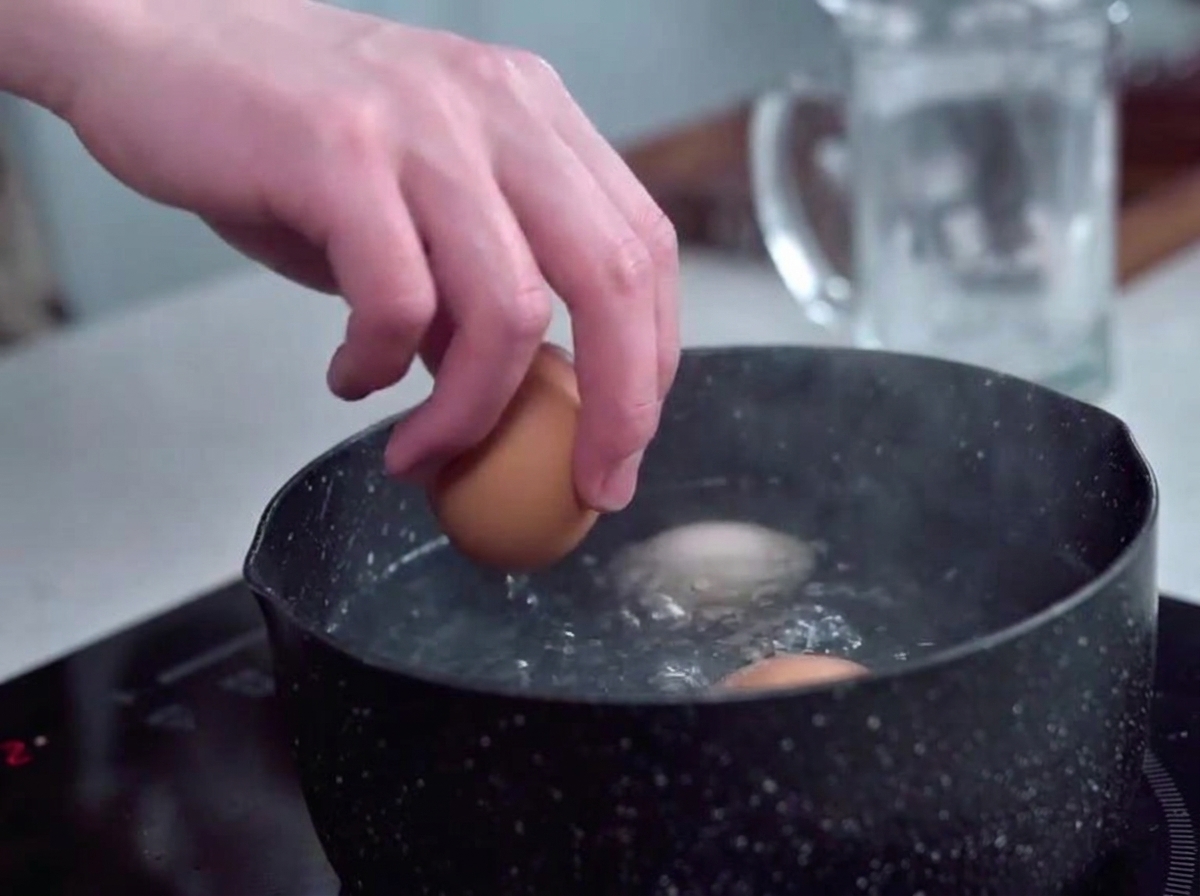 Eier werden vorsichtig mit der Hand in einen Topf mit sprudelnd kochendem Wasser gelegt.
