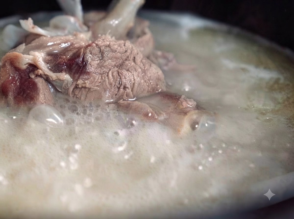 Eine dicke, milchige und undurchsichtige Schweineknochenbrühe, die kräftig in einem Topf kocht, mit sichtbaren Fleisch- und Knochenstücken.