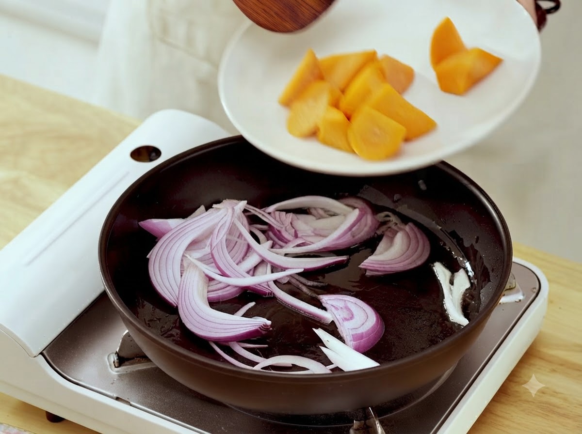 Karottenstücke werden von einem weißen Teller in eine Bratpfanne mit angebratenen Zwiebelstreifen gegeben.