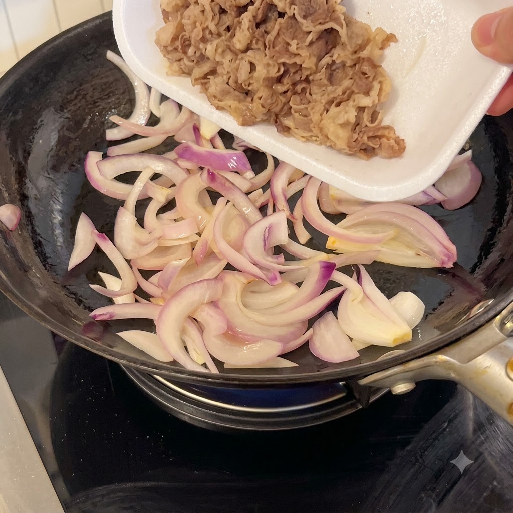 Dünn geschnittenes Rindfleisch wird aus einer weißen Schale in eine Pfanne mit angebratenen roten Zwiebeln gegeben.