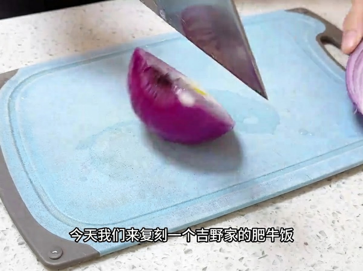Ein Küchenmesser schneidet eine rote Zwiebel auf einem blauen Schneidebrett in dünne Stücke.