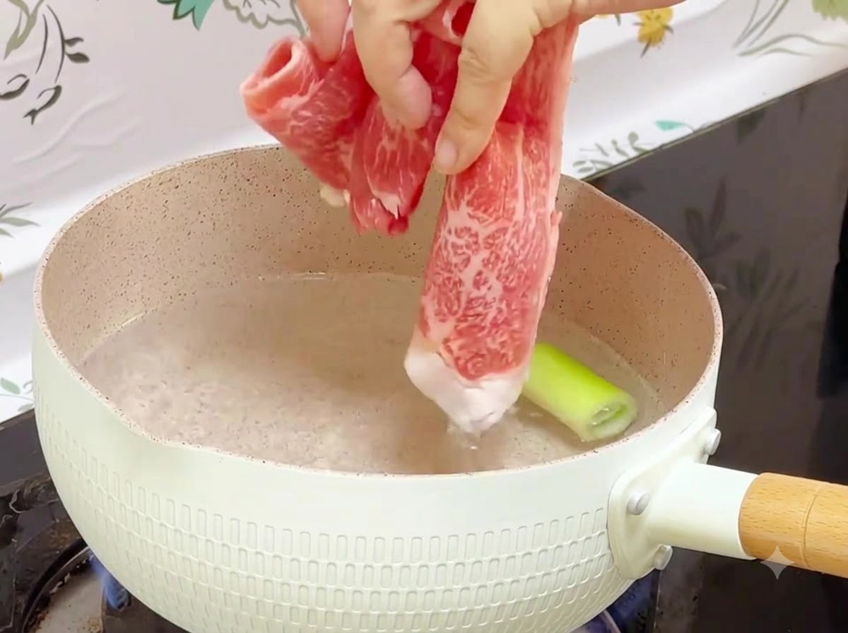 Gefrorene Rindfleischröllchen werden in einen Topf mit kochendem Wasser und einem Stück Frühlingszwiebel gegeben.