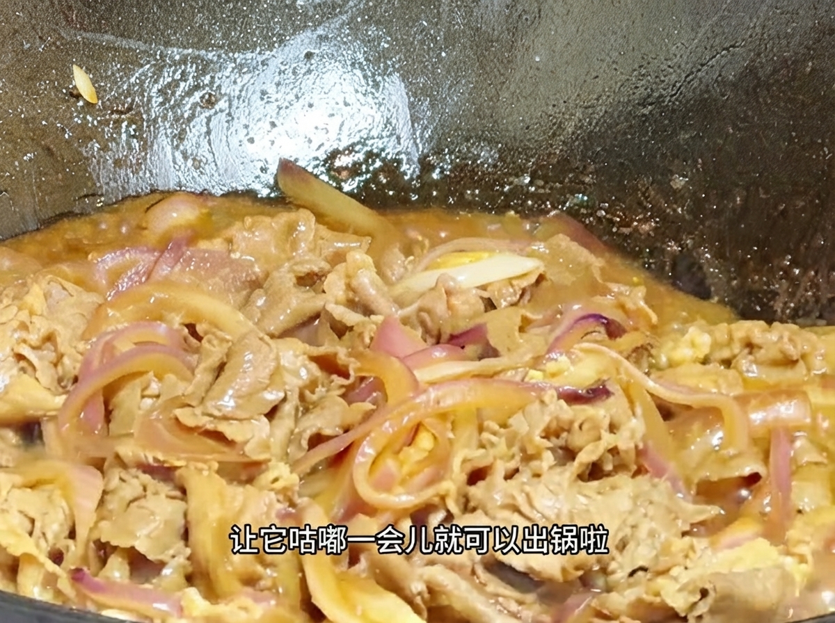 Nahaufnahme von Rindfleisch und Zwiebeln, die in einer eingedickten, blubbernden Sauce im Wok köcheln.