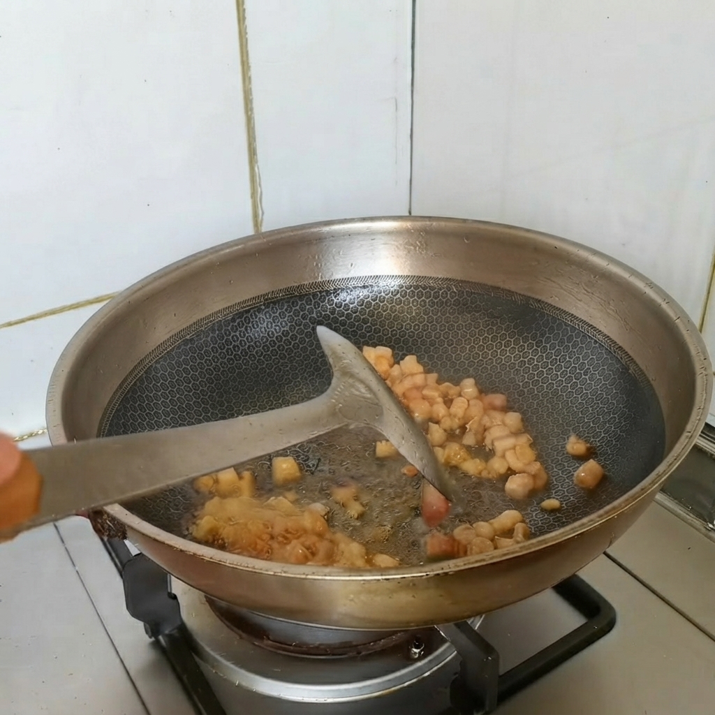 Anbratende Stücke von Schweinebauch werden im Wok mit Aromen pfannengerührt.