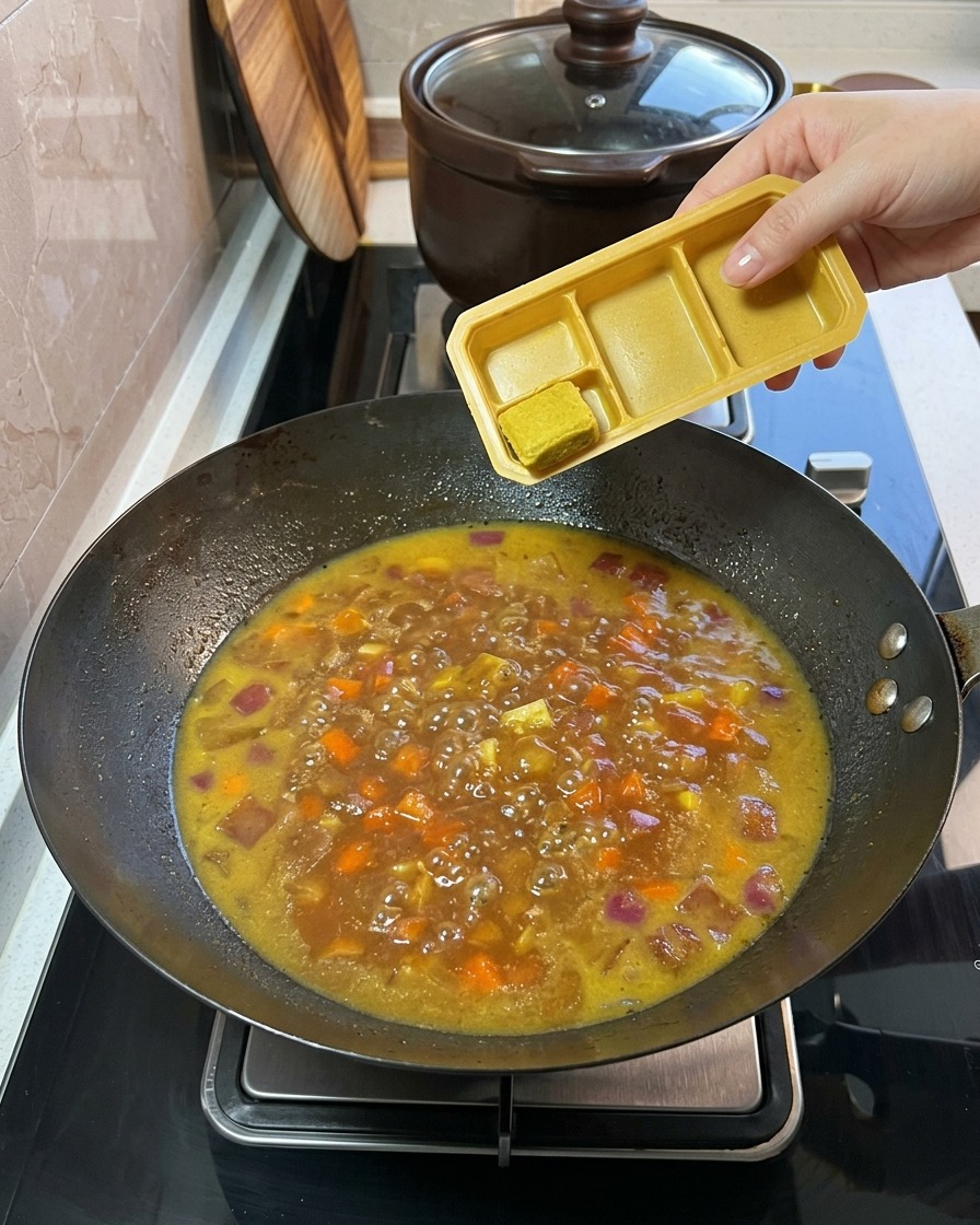 Feste Currywürfel werden aus einer Plastikschale in die köchelnde Gemüse-Brühe-Mischung gegeben.