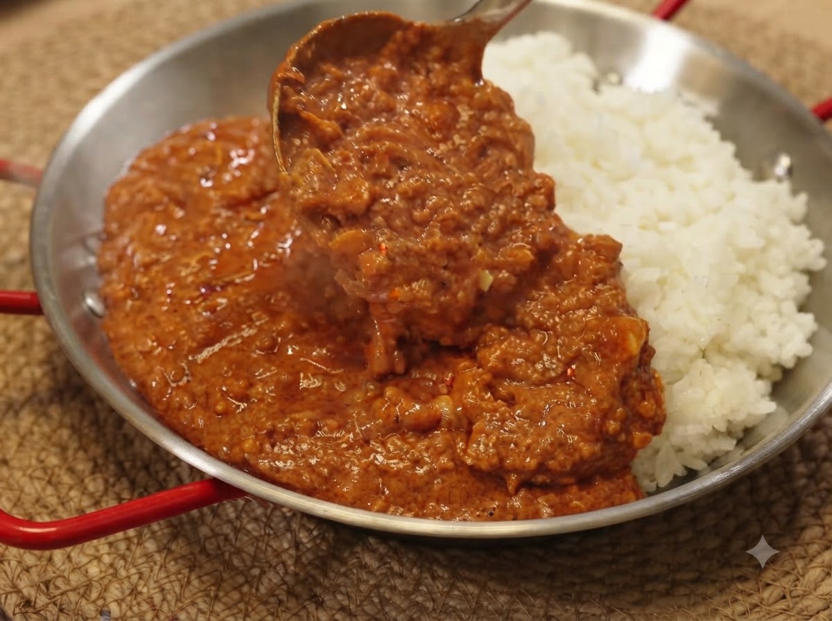Eine Kelle schöpft reichhaltige Curry-Hackfleisch-Sauce über ein Bett aus weißem Reis in einer Servierpfanne.