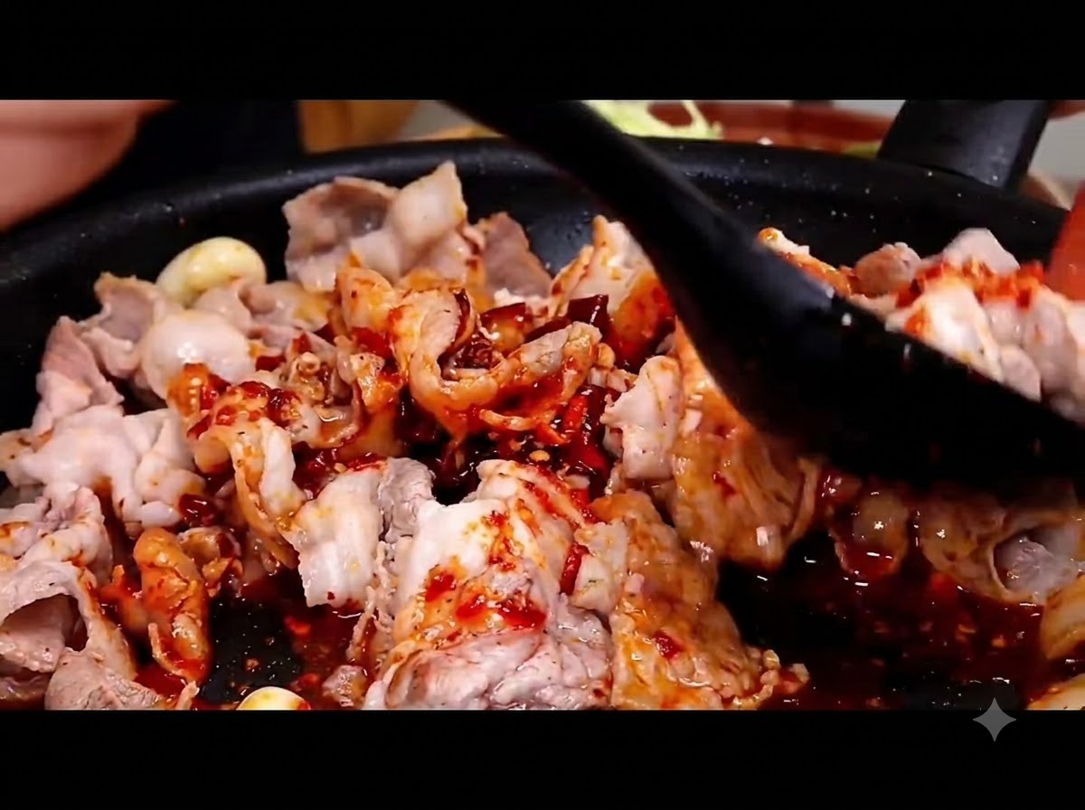 Ein schwarzer Pfannenwender mischt die scharfe rote Sauce unter die Schweinebauchscheiben in einer heißen Pfanne.