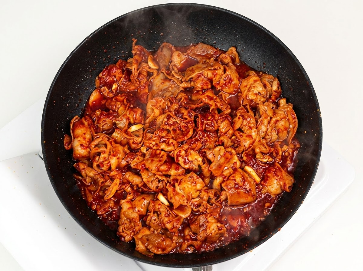Gestreifte weiße Zwiebeln werden zu dem gebratenen Schweinefleisch in der Pfanne gegeben.