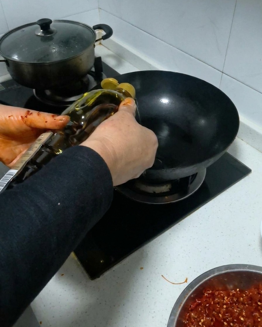 Speiseöl wird aus einer Flasche in einen schwarzen, vorgeheizten Wok gegossen.