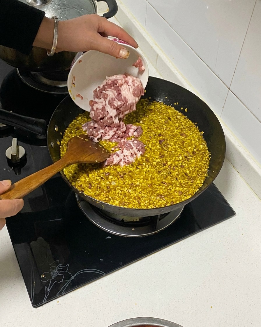 Gewürfelter Schweinebauch wird aus einer kleinen Schüssel in einen Wok mit angebratenen Aromen und Öl gefüllt.