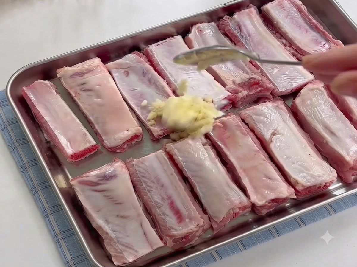 Ein Löffel gibt einen Berg frisch gehackten Knoblauchs auf rohe Schweinerippchen in einer Schale.