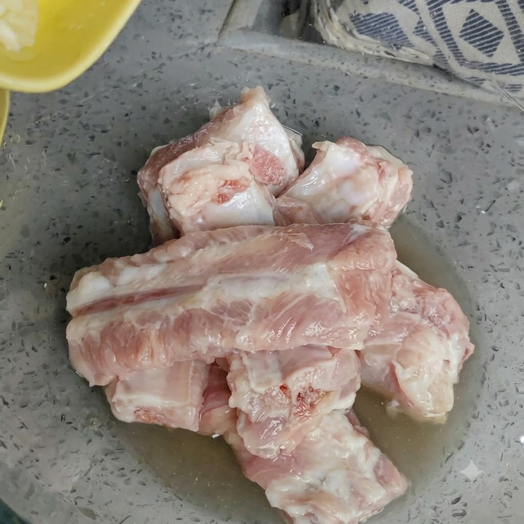 Schüssel mit rohen Schweinerippchen, auf die frisch gehackter Knoblauch gegeben wird.
