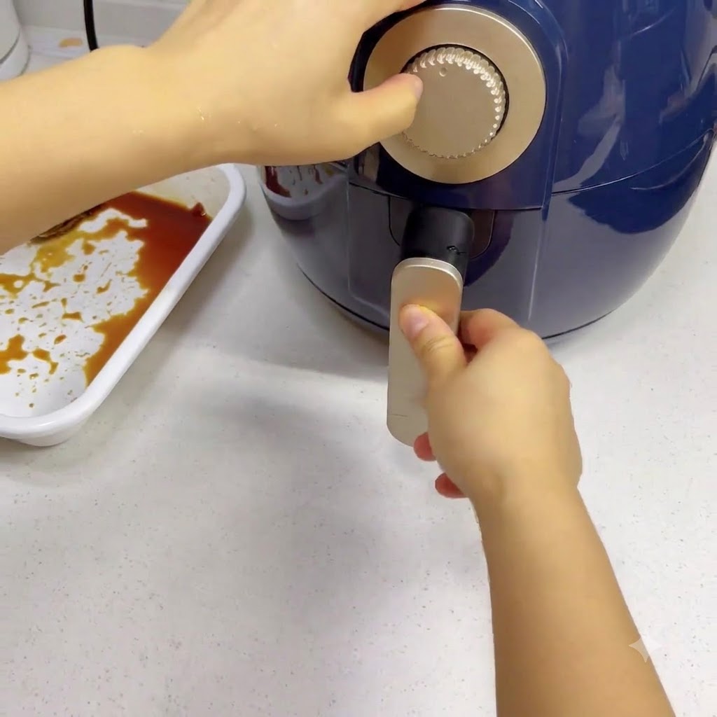 Eine Hand dreht den silbernen Timer-Regler an einer dunkelblauen Heißluftfritteuse.