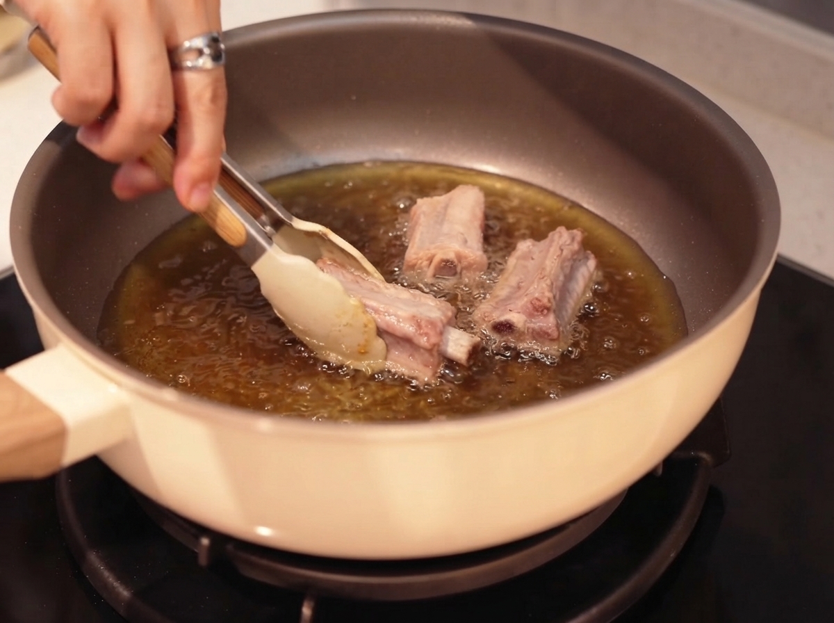 Schweinerippchen werden mit einer Zange in heißem Öl angebratencite: 1.