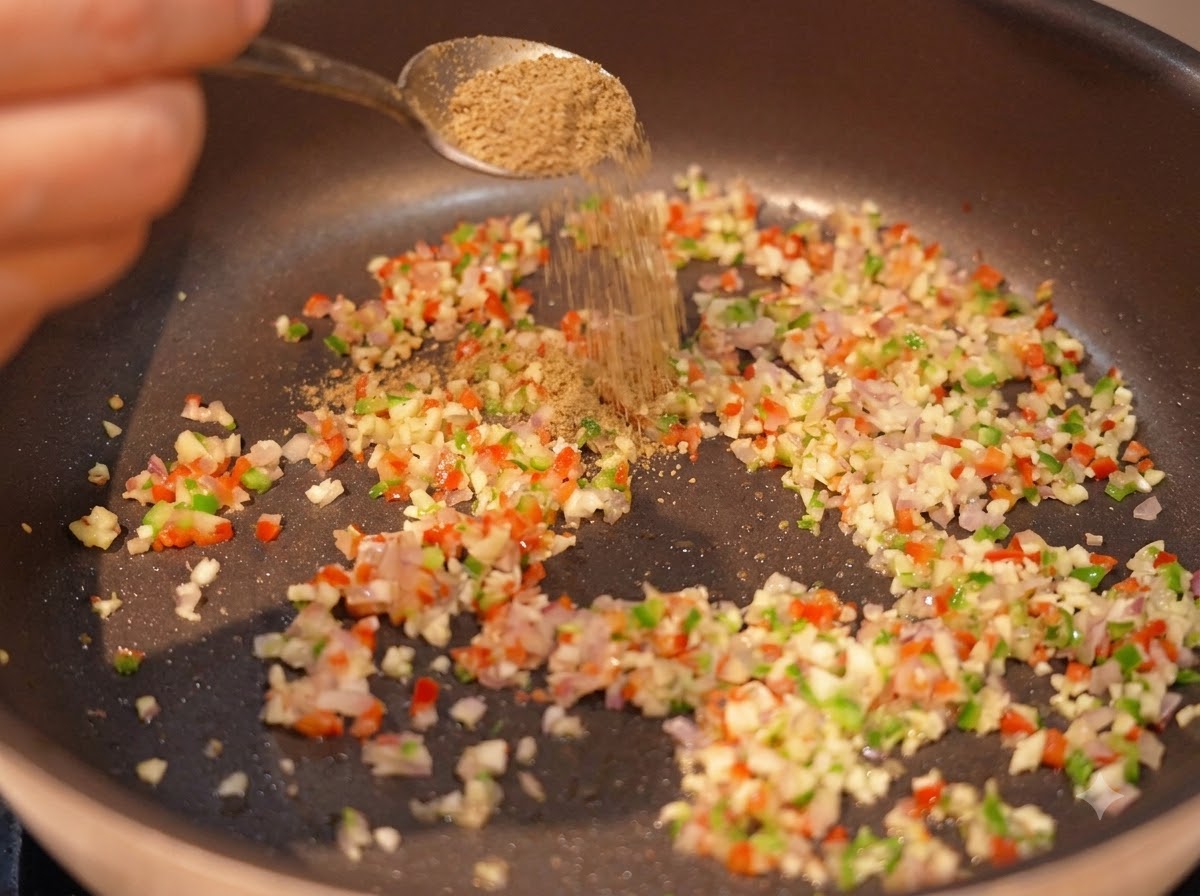 Kreuzkümmelpulver wird mit einem Löffel auf die angebratenen Aromaten in einer Pfanne gestreutcite: 1.