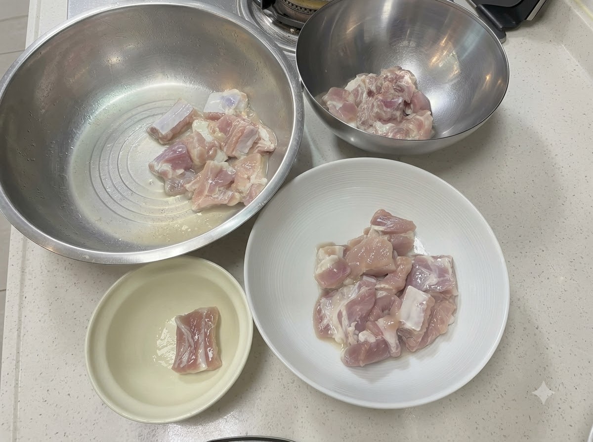 Schweinerippchenstücke angeordnet in verschiedenen Metall- und Keramikschüsseln auf einer weissen Arbeitsplatte.