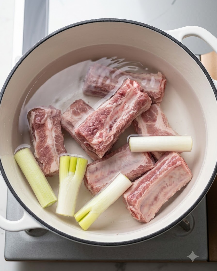 Frische Schweinerippchen in einem Topf mit kaltem Wasser, Frühlingszwiebeln und Aromaten vor dem Kochen.