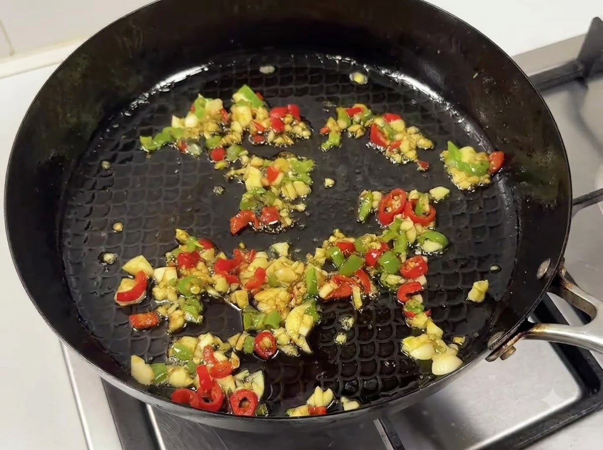 Eine Pfanne mit angebratenem Knoblauch, Chilis und einer herzhaften Saucenmischung.