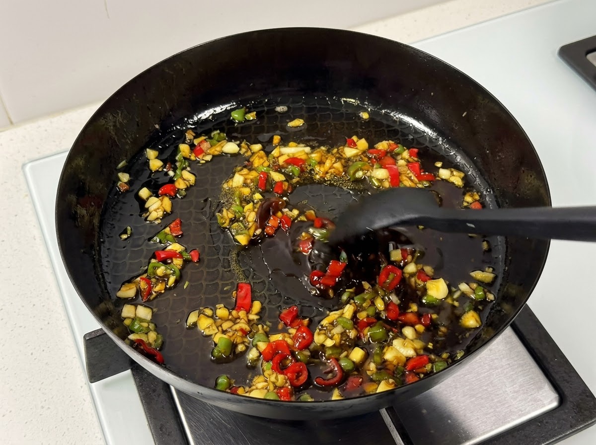 Ein Pfannenwender rührt Schweinerippchen und Sauce in einer Bratpfanne auf dem Herd.