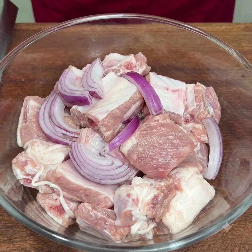 Geschnittene rote Zwiebel und Gewürze werden in einer Glasschüssel zu den rohen Rippchen gegeben.