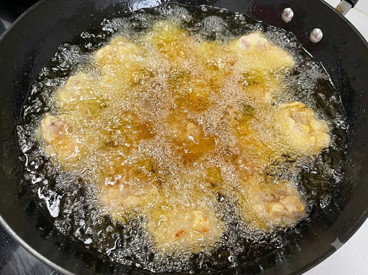 Mehrere Schweinerippchenstücke frittieren in heißem, blubberndem Öl in einem schwarzen Wok.