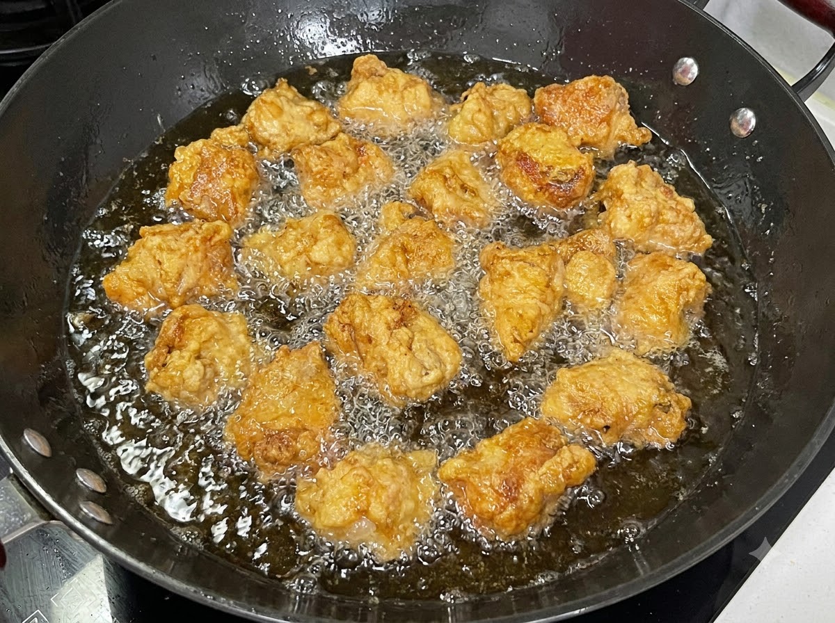 Stücke von panierten Schweinerippchen frittieren in einem schwarzen Wok voller blubberndem Öl.