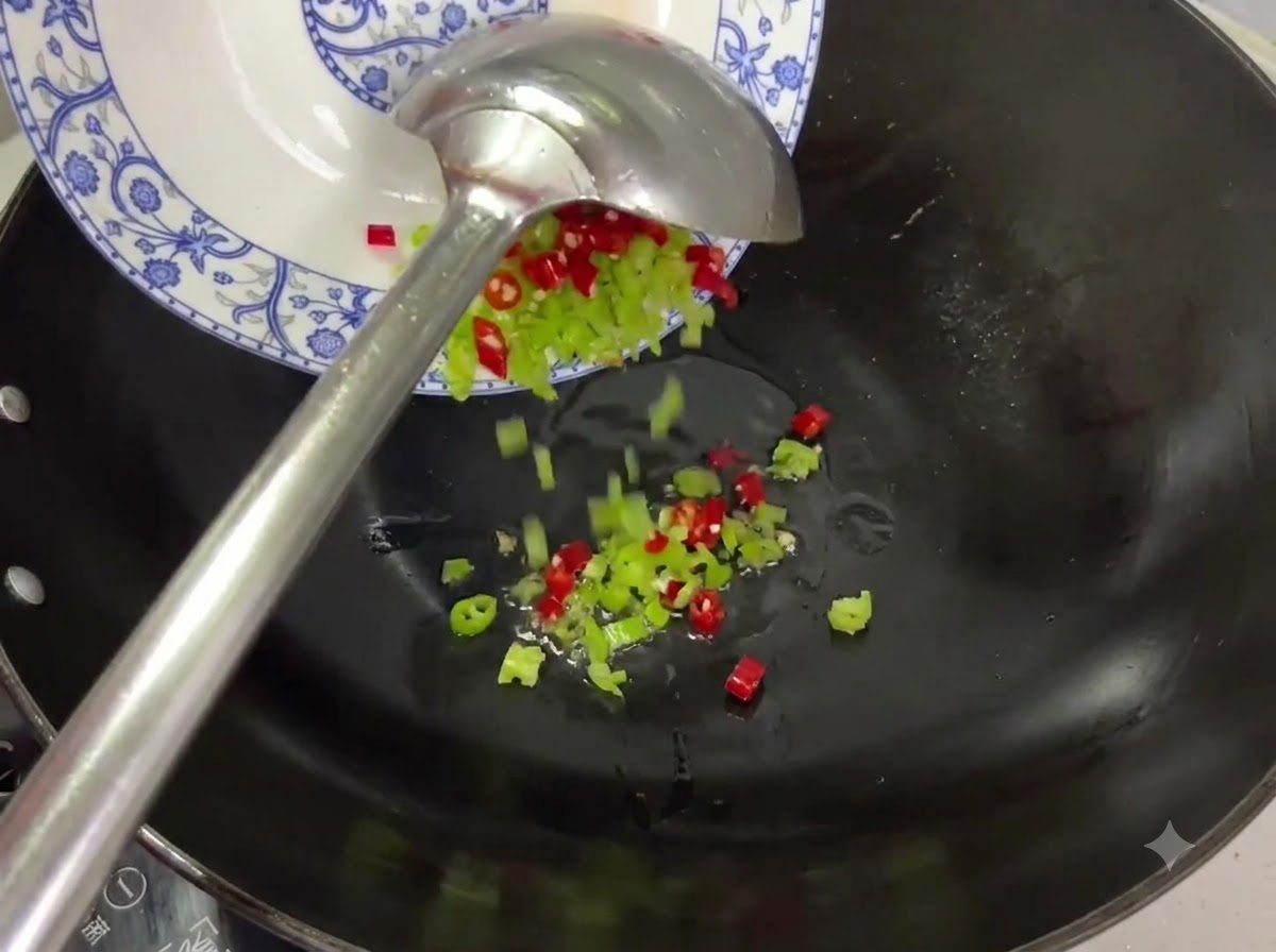 Rote und grüne Chilistücke werden von einem Teller in einen Wok mit Öl gegeben.