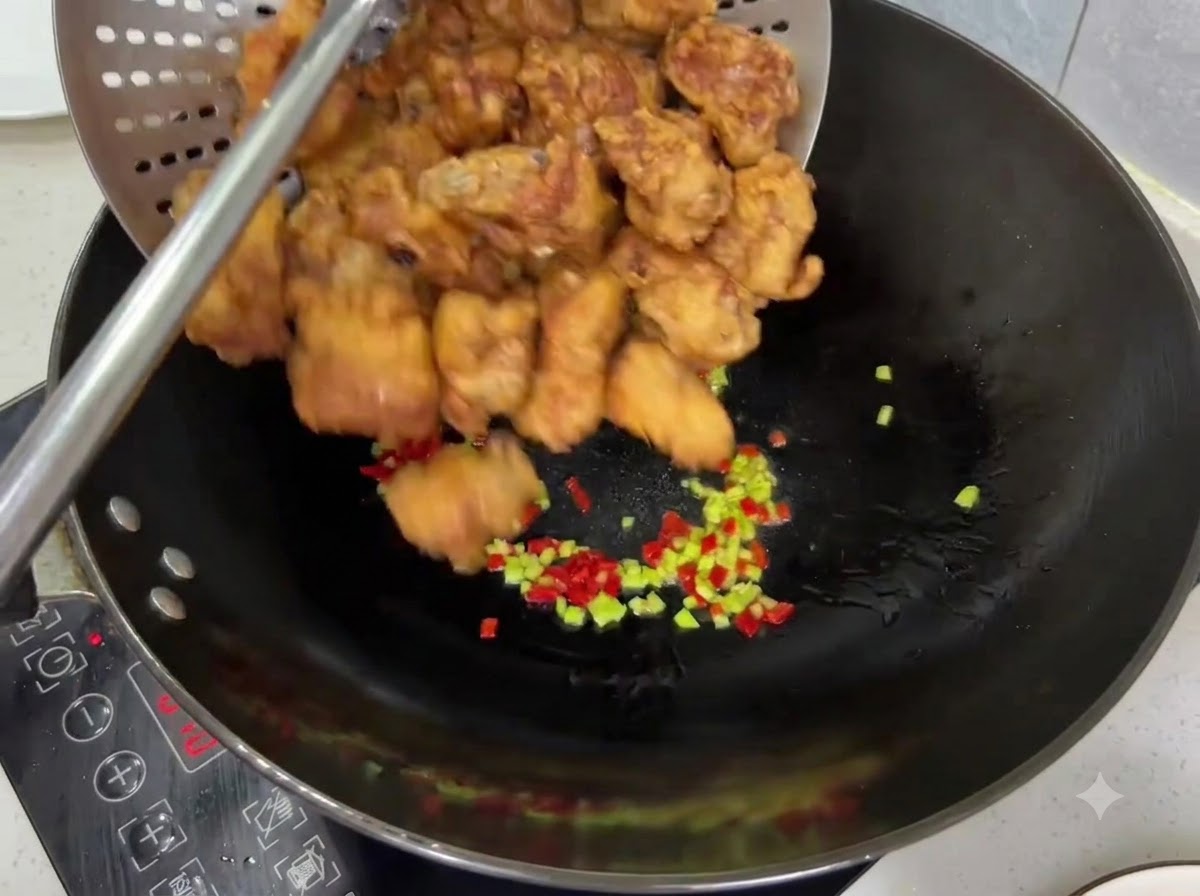 Knusprig goldbraun frittierte Schweinerippchen werden aus einem Sieb in einen Wok mit Chilis geschüttet.