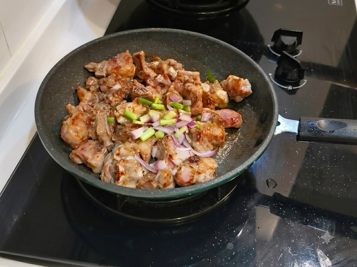 Gehackte Frühlingszwiebeln und Ingwer über den Schweinerippchen in der Bratpfanne verteilt.