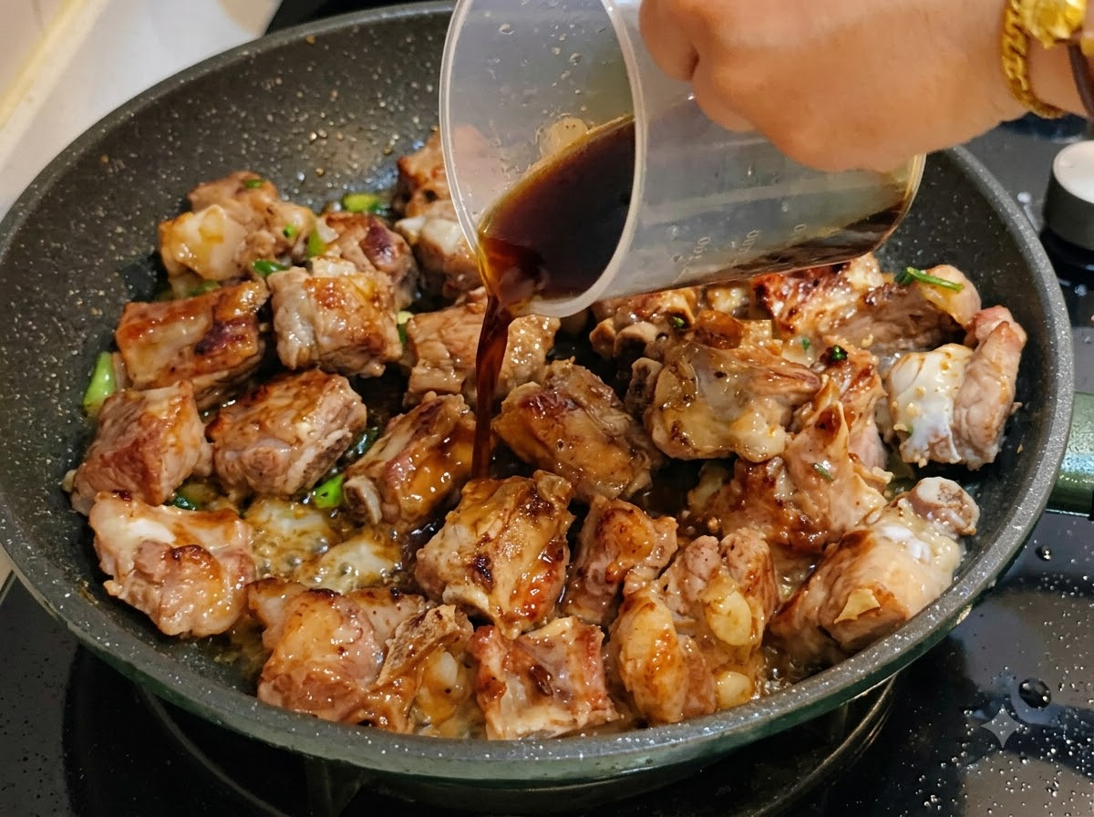 Dunkle Sauce wird aus einem Messbecher in die Pfanne mit den Schweinerippchen gegossen.