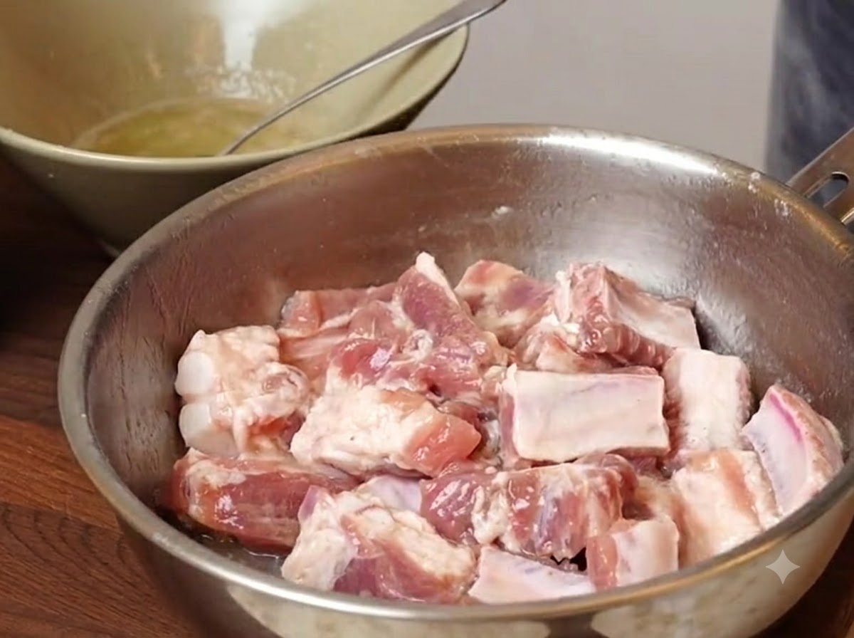 Schweinerippchenstücke liegen in einer Metallschüssel mit hinzugefügten Gewürzen und Stärken vor dem Mischen.