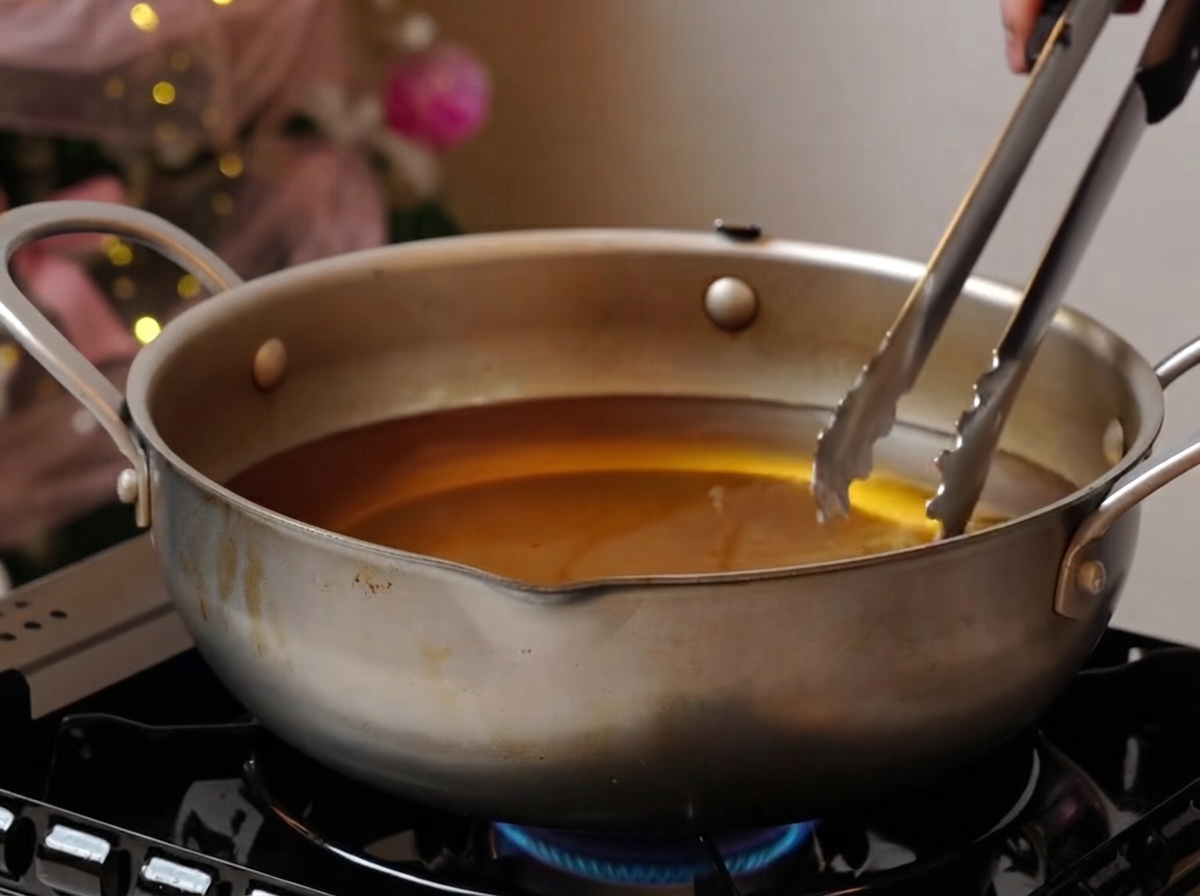 Schweinerippchen frittieren sanft in einem breiten Topf mit Öl über einer Flamme.
