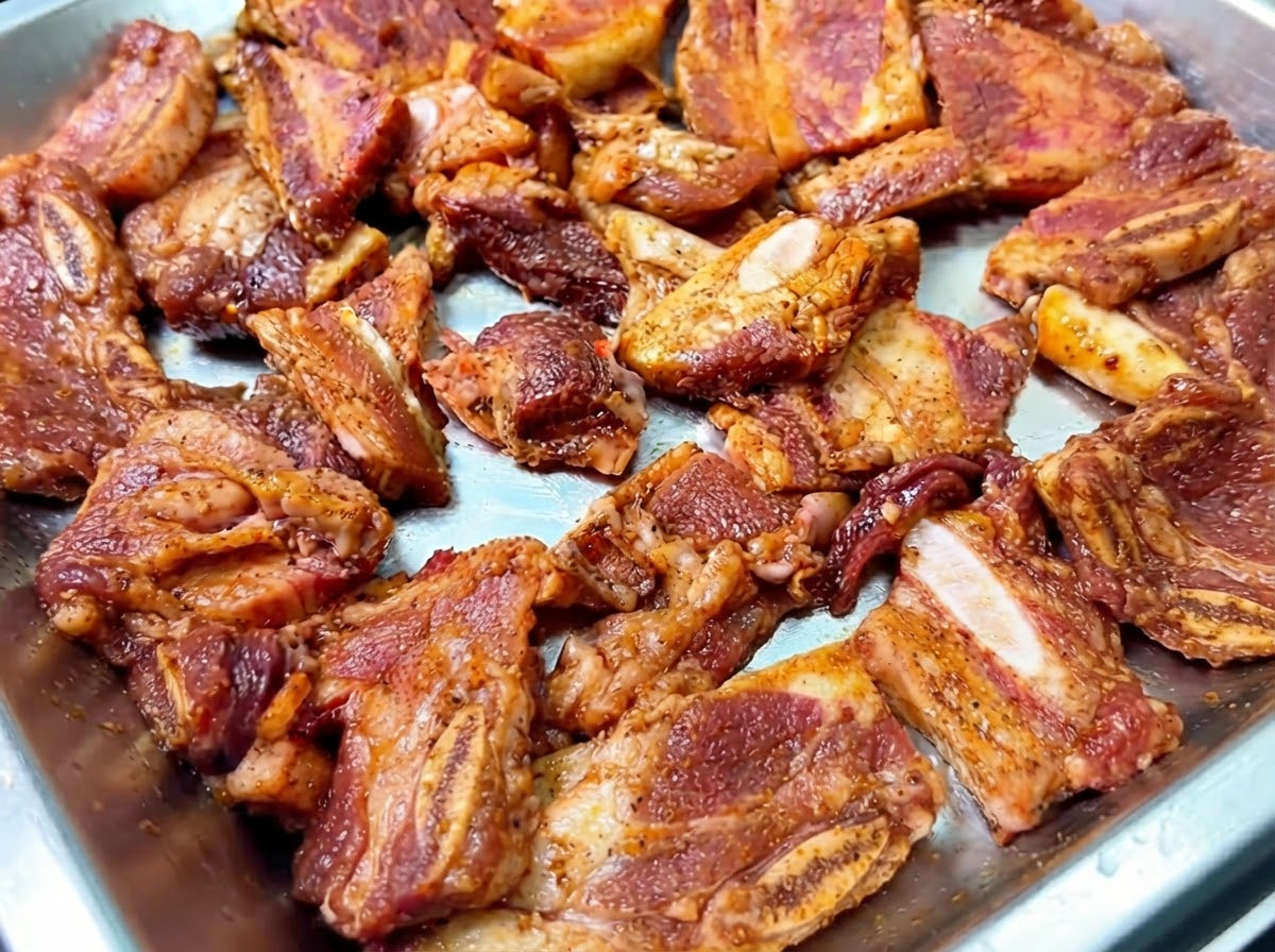 Marinierte Rinder-Short-Ribs in einer Metallschale, bestreut mit frischen Zwiebelstreifen.