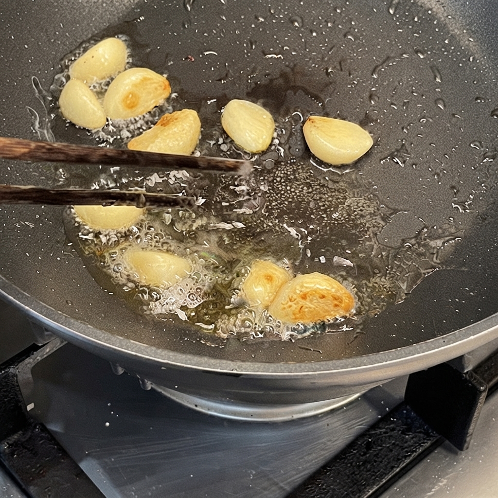 Knoblauchzehen werden mit Stäbchen in heißem Öl in einer Pfanne angebraten.