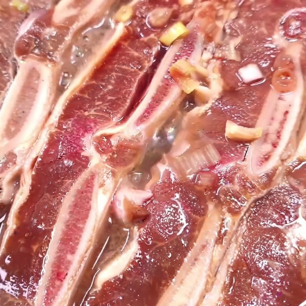 Rinderrippen kochen in einer Pfanne mit sprudelnd reduzierender Marinade.