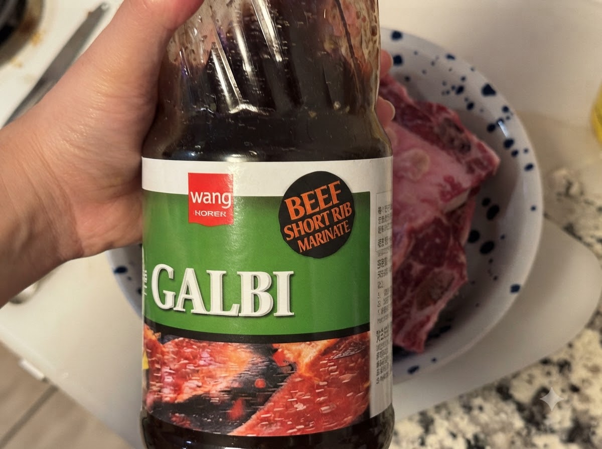 Eine Flasche koreanische BBQ-Galbi-Sauce wird in eine Schüssel mit rohen Rinderrippen gegossen.