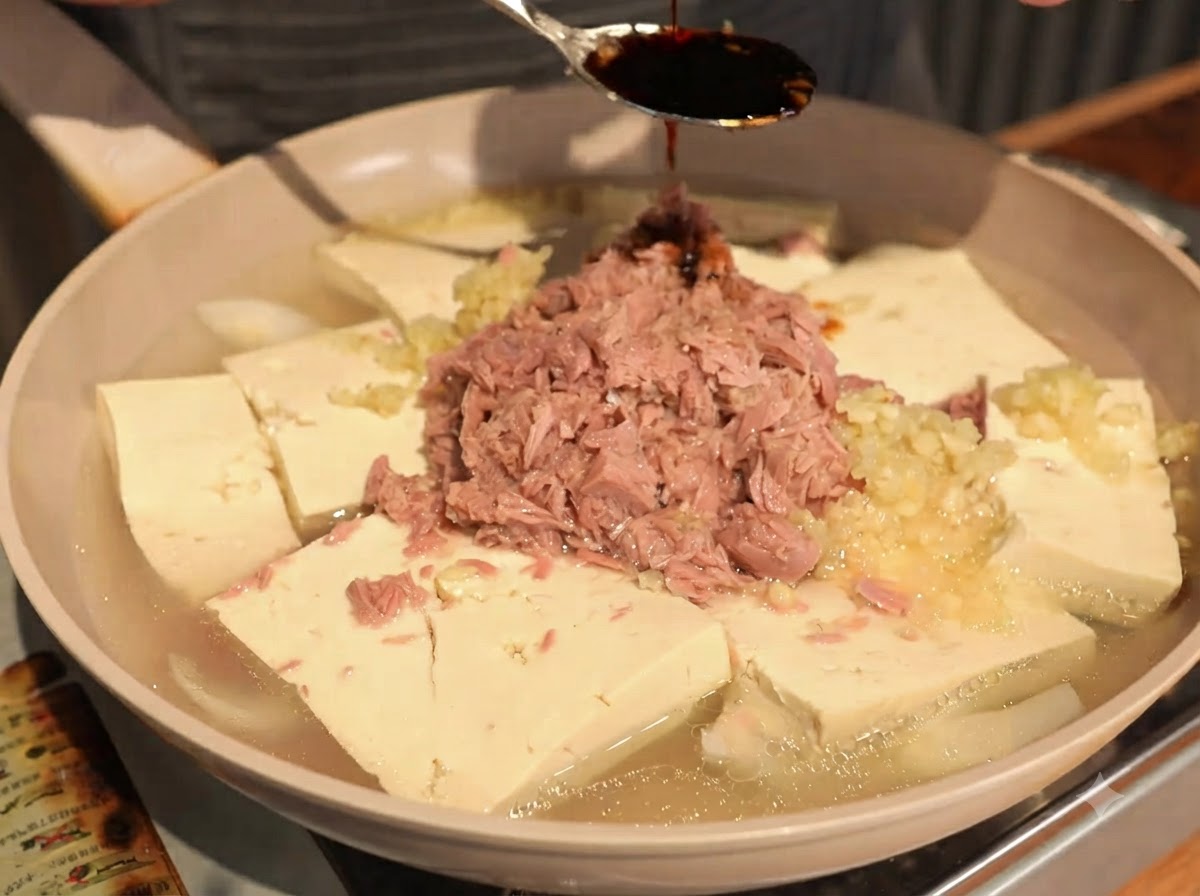 Dunkle Sojasauce wird von einem Löffel auf den Thunfisch und Tofu geträufelt.